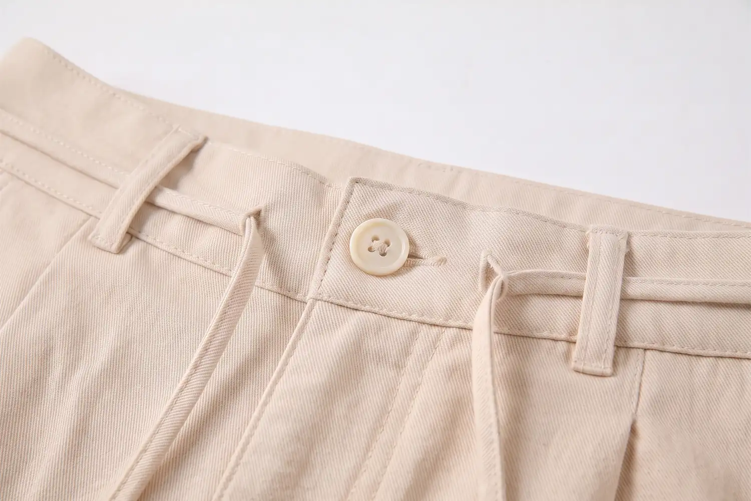 Close do cós da calça de linho, com as presilhas, o botão e o cordão passando por dentro.