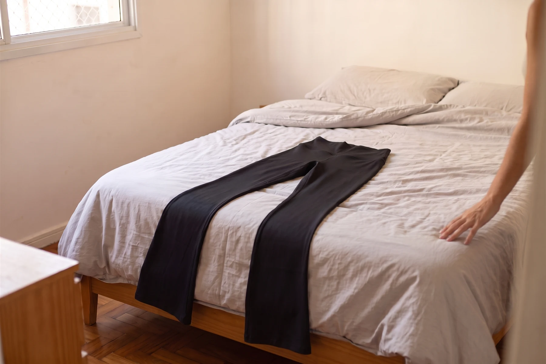 A calça legging flare preta estendida na cama, com a barra passando da beirada do colchão e encostando no chão.