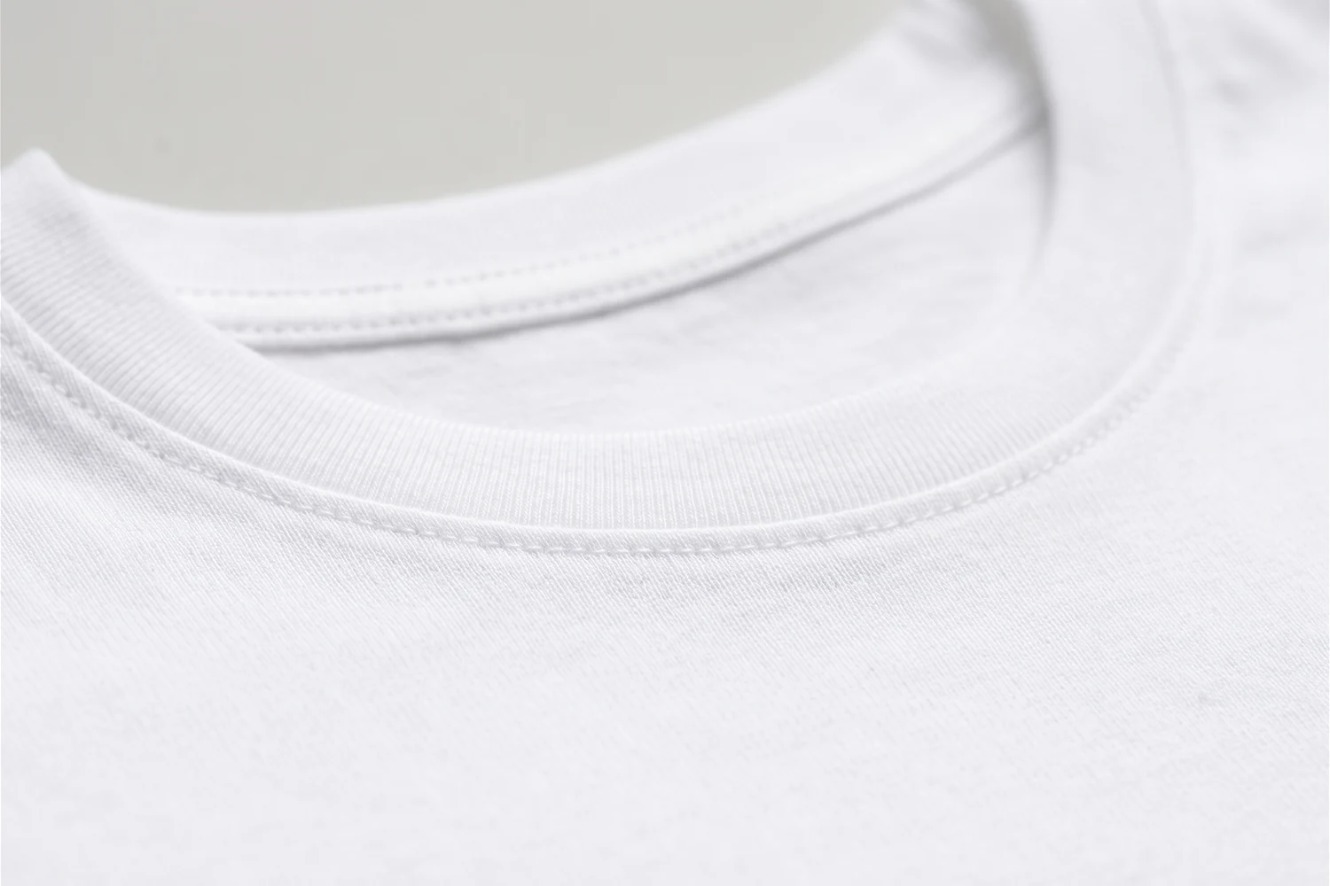Close da gola careca canelada da camiseta branca, com o pesponto onde ela encontra o corpo da peça.