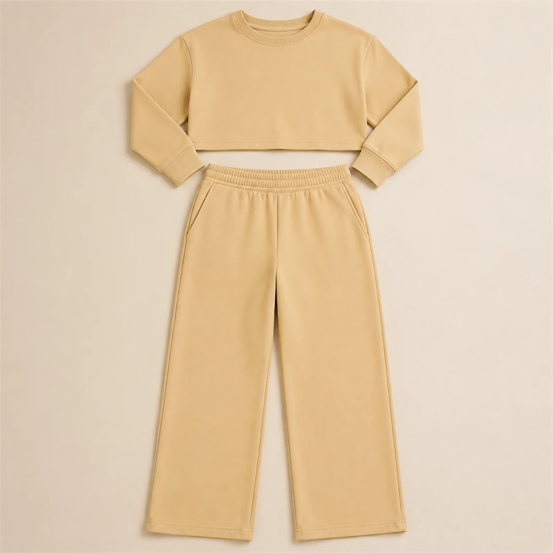 A blusa cropped de gola careca e a calça larga do conjunto de moletom, estendidas uma acima da outra e vistas de cima.