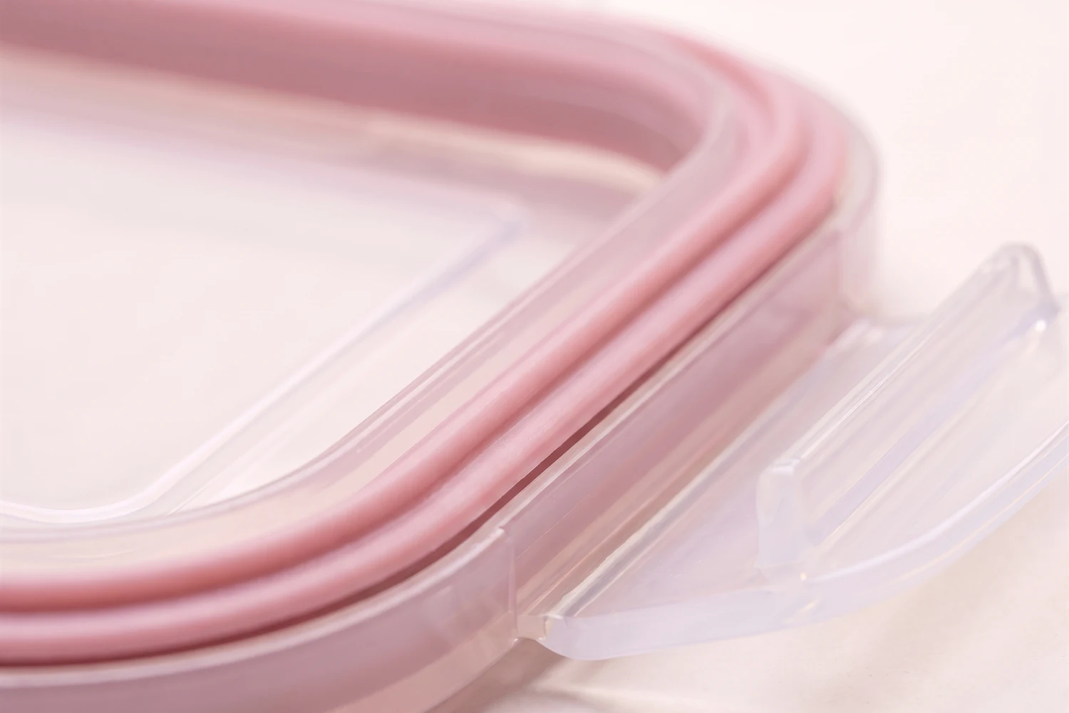 Close do anel de silicone rosa encaixado por dentro da tampa transparente, com uma trava lateral aberta.
