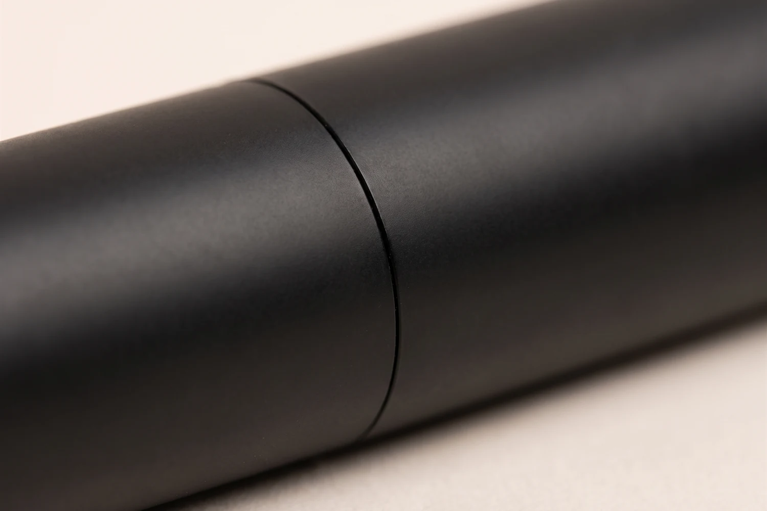 Close do tubo preto e liso da máscara de cílios, com a emenda entre a tampa e o corpo, sem nenhuma escrita.