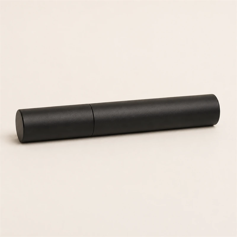 Um tubo de máscara de cílios preto e fechado, deitado em fundo neutro, sem rótulo.