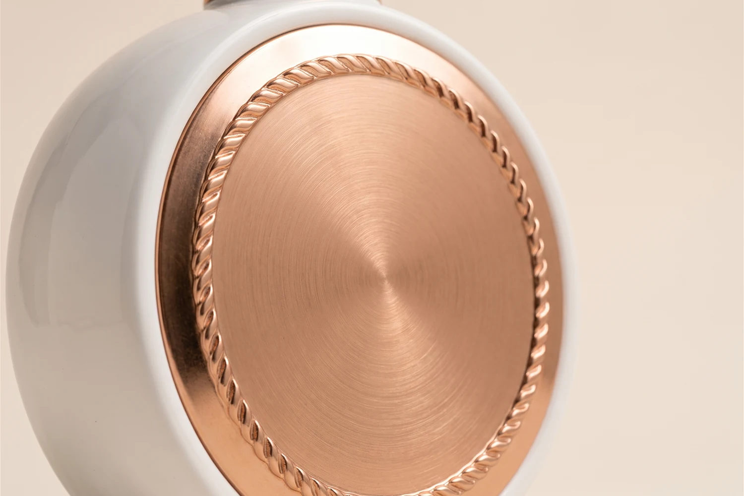 Close do disco de metal rosé escovado aplicado na frente do frasco branco, com o cordão em relevo em volta.