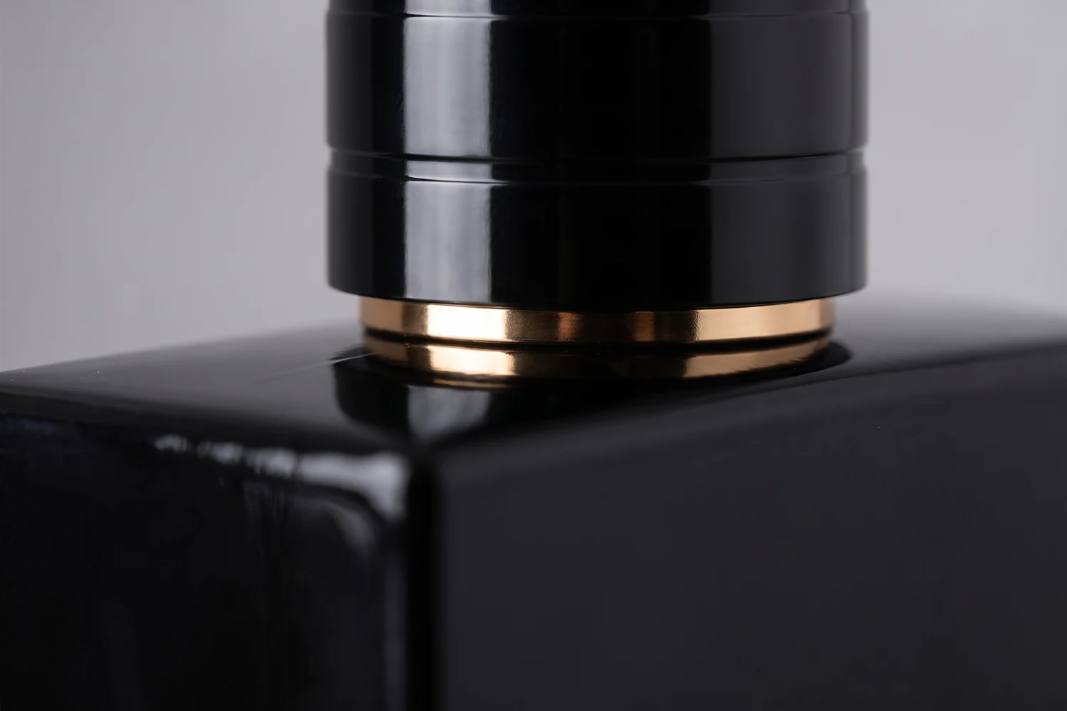 Close do aro dourado na base da tampa preta do perfume, apoiada no ombro do frasco.